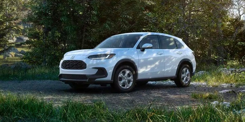 A photo of a white 2024 Honda HR-V parked in a shady patch of grass.