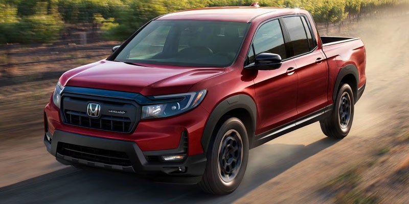 A photo of a red 2024 Honda Ridgeline driving down a dirt road