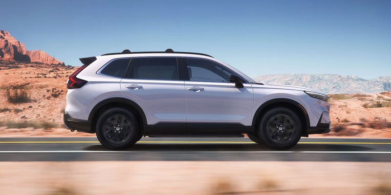 A photo of a white 2025 Honda CR-V Hybrid driving down a dessert road.