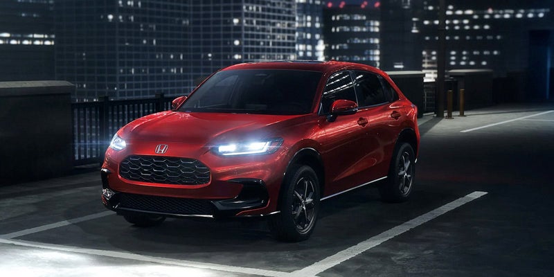 A red 2025 Honda HR-V driving down a city street at night.