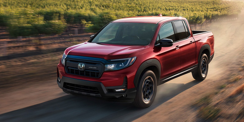 A photo of a red 2025 Honda Ridgeline driving down a dirt road.